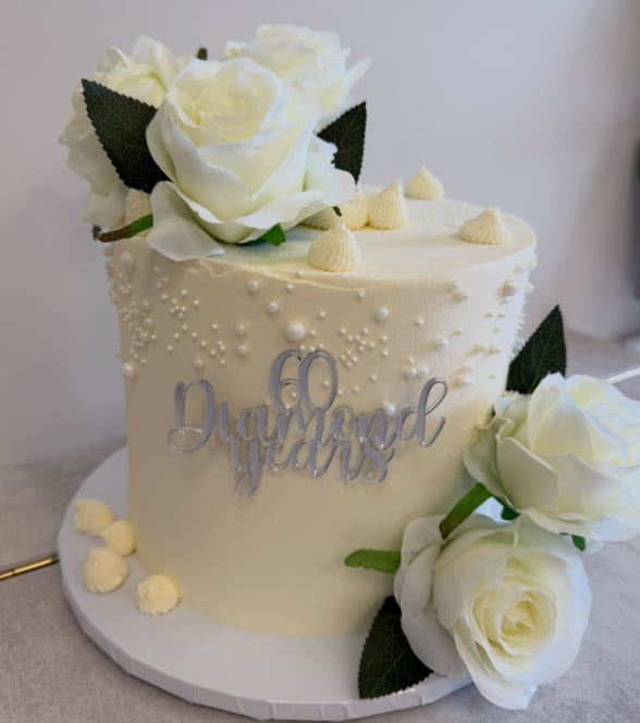 An ivory buttercream cake covered in sugar pearls with white roses and a silver "60 Diamond Years" topper