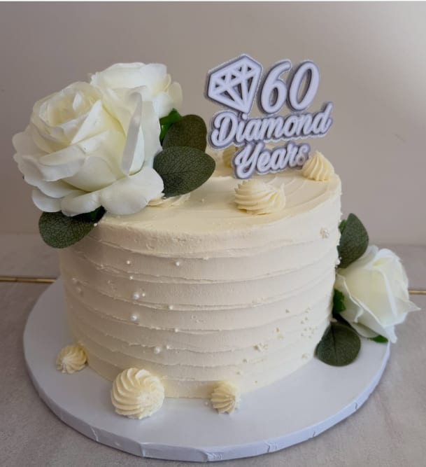 A tall ivory buttercream cake with combed texture, silk roses and a "60 Diamond Years" topper